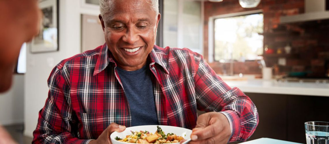 a patient smiling as he eats his food out of a bowl at a dining table because PRF was used to accelerate the healing process of his dental implant procedure.