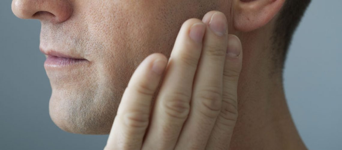 a picture of a patient holding his jaw where he needs a tmj treatment.