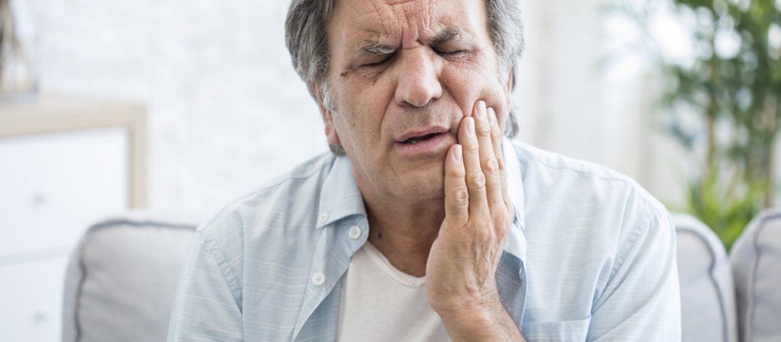 a man in discomfort, holding his jaw because of dental implant pain